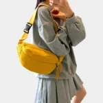 Sac banane velours côtelé jaune porté en bandoulière par une femme, avec sangle à motif rayé et boucle plastique