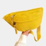 Sac banane velours côtelé jaune posé de face dans une main, avec zip et cordons tressés ton sur ton
