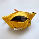 Sac banane velours côtelé jaune posé vu de dessus, poche principale ouverte avec essentiels visibles à l’intérieur