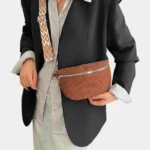 Sac banane velours côtelé marron porté en bandoulière par une femme au style chic, avec sangle à motif géométrique