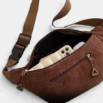 Sac banane velours côtelé marron posé de face vu de dessus, poche principale ouverte contenant un smartphone