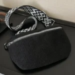 Sac banane velours côtelé noir posé à plat, vue de face avec sangle large à motif ethnique géométrique