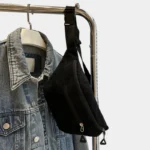 Sac banane velours côtelé noir posé de côté sur un cintre, avec sangle noire et clips en plastique