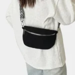 Sac banane velours côtelé noir porté en bandoulière par une femme au style chic avec sangle à motif géométrique