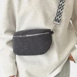 Sac banane velours côtelé noir porté en bandoulière par une femme au style chic avec sangle à motif géométrique