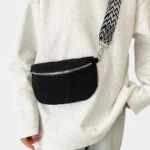 Sac banane velours côtelé noir porté en bandoulière par une femme avec sangle à motif graphique