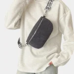 Sac banane velours côtelé noir porté en bandoulière par une femme avec une sangle motif chevron au style chic