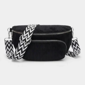 Sac banane velours côtelé noir profond posé de face, avec sangle à motif zigzag noir et blanc
