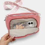 Sac banane velours côtelé rose présenté à plat vue de face, poche avant ouverte révélant une doublure chevronnée claire et un téléphone