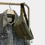 Sac banane velours côtelé vert kaki posé de face sur un cintre, avec fermeture éclair argentée