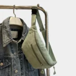 Sac banane velours côtelé vert pâle posé en suspension de face, avec sangle unie et boucle plastique