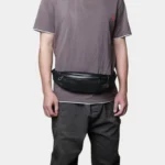 Petit sac banane cuir noir porté à la taille par un homme de face