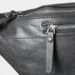 Grand sac banane cuir noir en gros plan de face, avec fermeture zippée chromée et languette en cuir