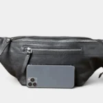 Grand sac banane cuir noir posé de face, avec poche avant zippée et un smartphone placé devant