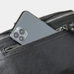 Grand sac banane cuir noir posé de face, poche avant ouverte contenant un smartphone