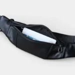 Petit sac banane en cuir noir vu de face avec la poche principale ouverte contenant des cartes bancaires