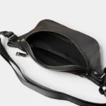 Sac Banane Cuir Vintage Homme Sac banane cuir noir posé vu de dessus, poche principale ouverte révélant poches zippées intérieures