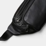 Sac Banane Cuir Noir Homme Souple Sac banane cuir noir posé en biais, gros plan sur la texture souple et les zips métalliques chromés