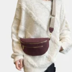 Sac banane bordeaux en simili cuir porté en bandoulière par une femme au style chic avec sangle tressée