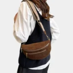 Sac banane marron en simili daim porté en bandoulière par une femme, avec sangle à motif beige au style chic
