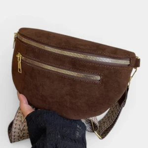 Sac banane marron foncé au style chic en simili cuir effet daim, posé de face dans une main avec sangle à motif chevron