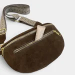 Sac banane marron en daim posé de face, poche avant ouverte contenant un tube, avec sangle à motif chevron