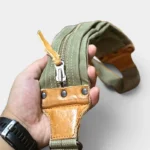 Sac banane kaki en coton et cuir porté en main par un homme, gros plan sur la fermeture à glissière métallique