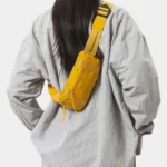 Petit sac banane nylon jaune porté en bandoulière dans le dos par une femme au style décontracté-chic