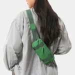 Petit sac banane nylon vert porté en bandoulière dans le dos par une femme au style décontracté-chic, vue de dos