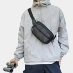 Sac banane nylon ripstop à carreaux noir porté en bandoulière par un homme, randonneur tenant des jumelles
