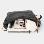Sac banane nylon quadrillé noir, poche principale ouverte révélant un smartphone et divers essentiels