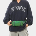 Petit sac banane nylon vert porté à la taille par une femme de face au style streetwear