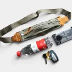 Sac banane en toile coton vert kaki et cuir, posé de face avec fermeture zippée, accompagné d'affaires essentielles
