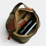 Sac banane vert kaki en cuir et toile au style militaire, poche principale ouverte contenant portefeuille et smartphone vu de dessus