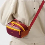 Sac Banane Colorblock Multicolore Compact Sac banane colorblock en nylon bordeaux et orange porté en bandoulière par une femme au style casual-chic, de face