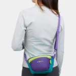 Sac banane colorblock en nylon violet, vert et turquoise porté en bandoulière de dos par une femme
