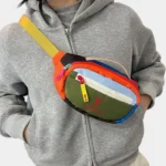 Petit sac banane nylon multicolore colorblock porté en bandoulière par une femme au style streetwear décontracté