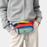 Petit sac banane nylon multicolore porté à la taille par un homme, de face au style streetwear
