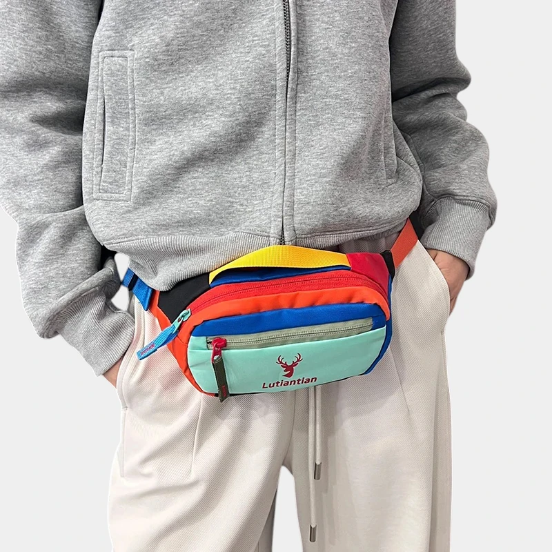 Petit sac banane nylon multicolore porté à la taille par un homme, de face au style streetwear