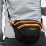 Sac banane nylon noir porté en bandoulière de face, avec fermeture éclair jaune et orange