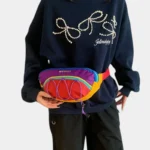 Sac banane multicolore aux couleurs vives tenu à la taille par une femme au style streetwear
