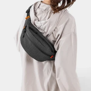 Sac banane nylon quadrillé noir porté en bandoulière croisée par une femme au style sport-outdoor, de profil