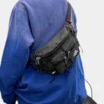 Sac Banane Nylon Ripstop Technique Outdoor Sac banane nylon à motif quadrillé noir et gris, porté en bandoulière dans le dos par une personne au style streetwear