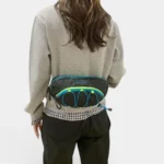Sac banane outdoor noir porté à la taille par une femme, vue de dos, avec élastiques bleus et jaunes fluo