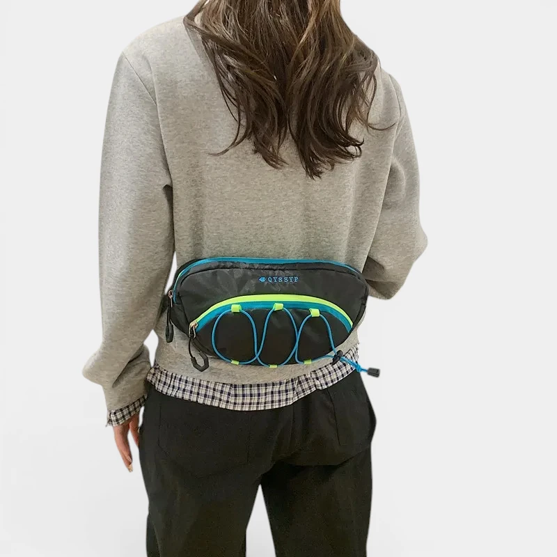 Sac banane outdoor noir porté à la taille par une femme, vue de dos, avec élastiques bleus et jaunes fluo