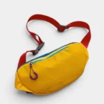 Sac banane multicolore outdoor posé de face, avec sangle rouge et fermeture éclair turquoise sur fond jaune vif
