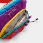 Sac banane multicolore outdoor vu en gros plan, poche principale ouverte révélant un rouge à lèvres et un fond de teint