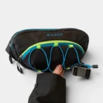 Sac banane outdoor noir tenu à la main, vue de face avec élastiques bleu et vert sur le panneau avant