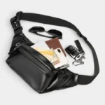 Sac banane en simili cuir noir, poche principale ouverte révélant un smartphone et des essentiels