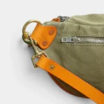 Sac Banane Toile Kaki Militaire Bandoulière Cuir Véritable Sac banane en toile kaki vu en gros plan sur le côté, avec une bandoulière en cuir orange et un mousqueton doré
